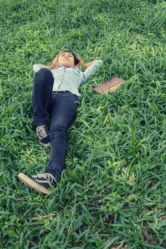 Young hipster woman lying down on grass when she tired after read book. photo