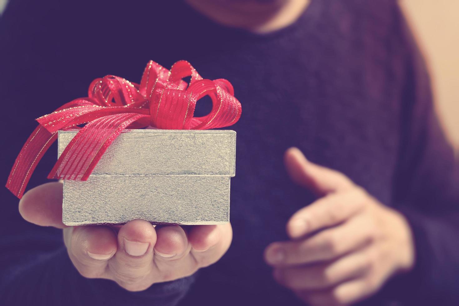 entrega de regalos, mano de hombre sosteniendo una caja de regalo en un gesto de dar. fondo borroso, efecto bokeh foto