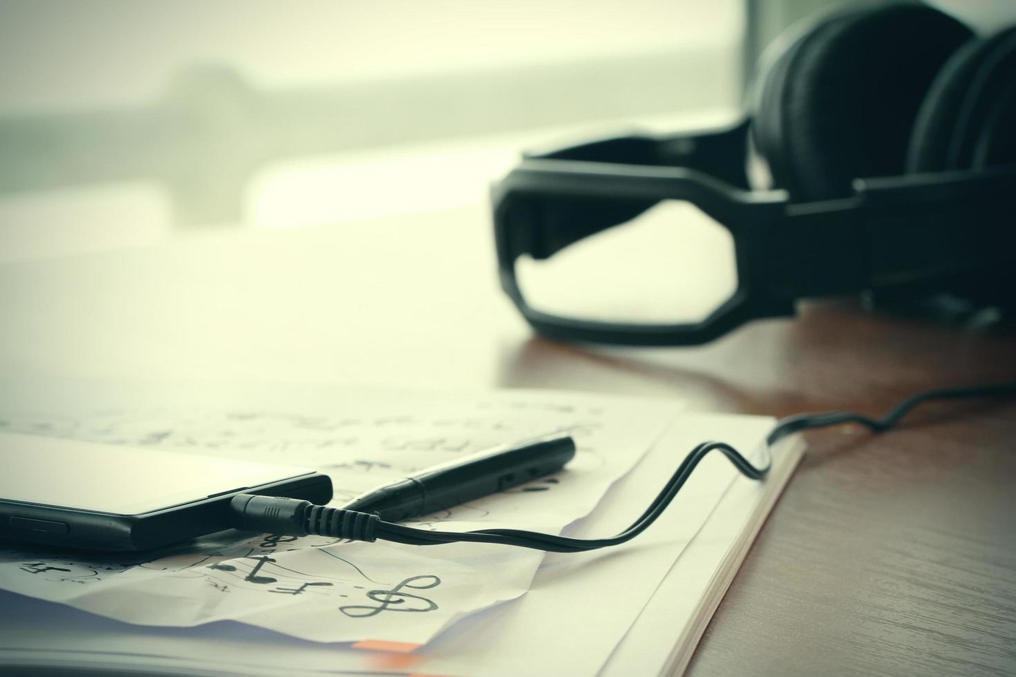 Closeup jack of smart phone with headphone on musical notes paper with shallow DOF evenly matched on wooden desk photo