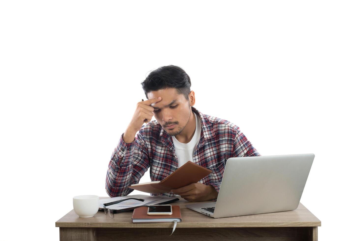 Thoughtful young man holding pen looking at notepad while sitting at his working place. photo