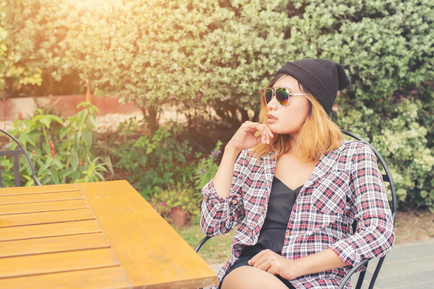 Outdoor portrait of young hipster woman sitting alone at old city cafe and waiting for her boyfriend wearing plaid outfit and  sunglasses. photo