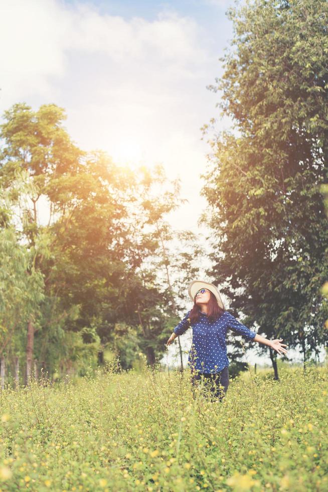 atractiva mujer joven de pie en un campo de flores amarillas, manos esparcidas y disfrutando del refrescante entorno natural. foto