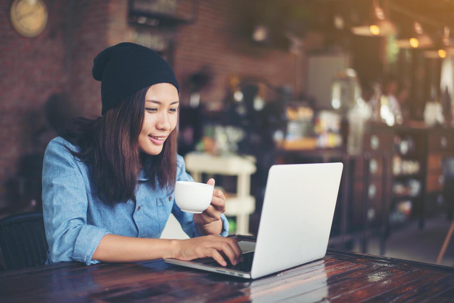 hermosa joven hipster sentada en una cafetería, relájese y juegue con su laptop, encuentre información sobre el tiempo libre, feliz y divertido. concepto de estilo de vida. foto