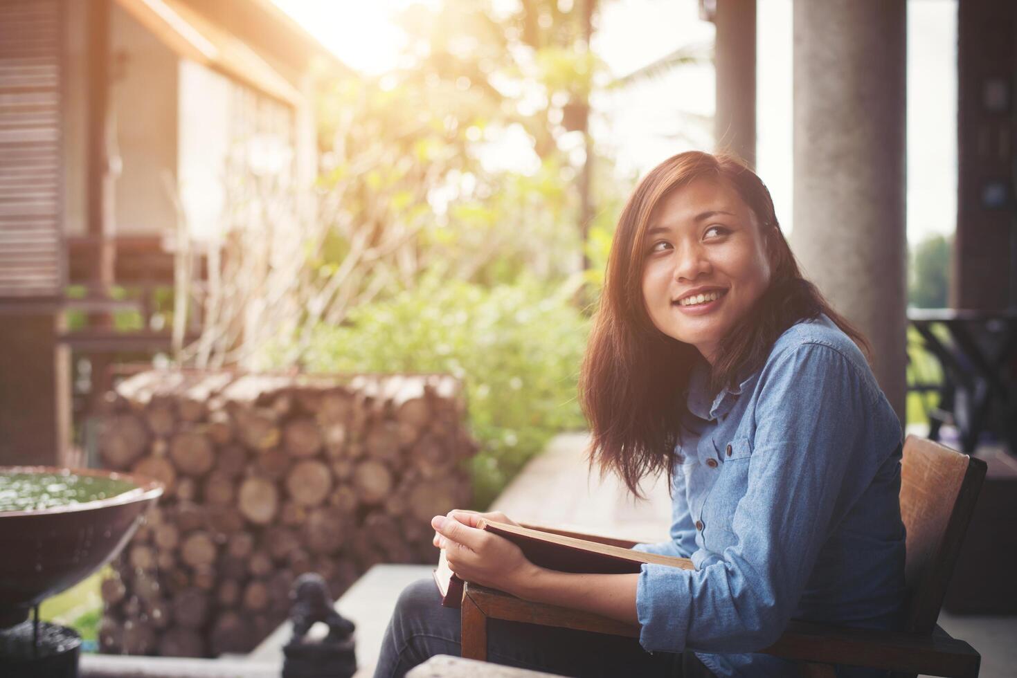 mujer joven leyendo un libro sentado en la silla. vacaciones relajantes disfrutar de la lectura. foto