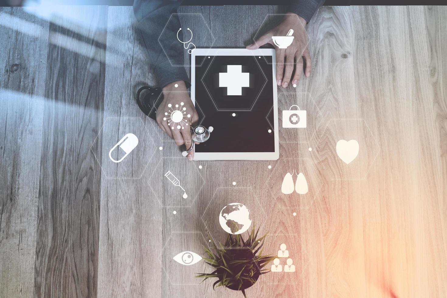 médico que trabaja con una tableta digital y un estetoscopio en un escritorio de madera en el hospital con una interfaz de pantalla de iconos virtuales foto