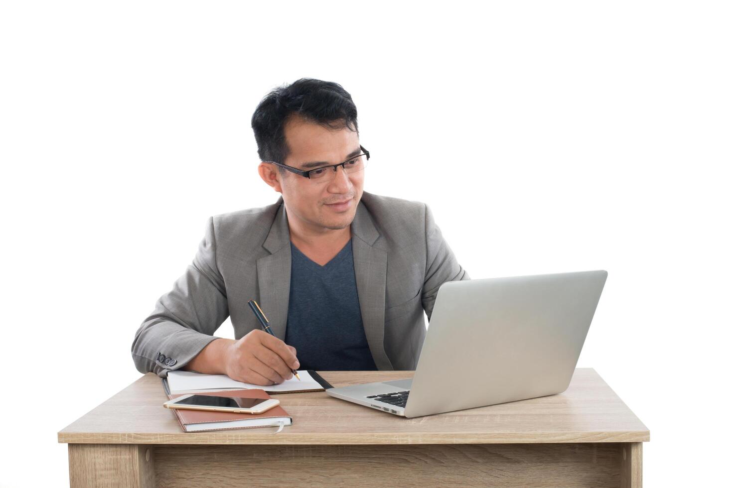 businessman writing notes on a writing pad while sitting at his desk behind his new notebook isolated on white background. photo