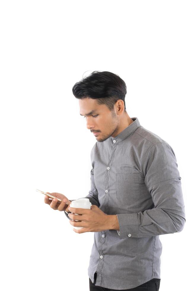 joven hipster mirando su teléfono inteligente mientras la taza de café en las manos está aislada en el fondo blanco. foto