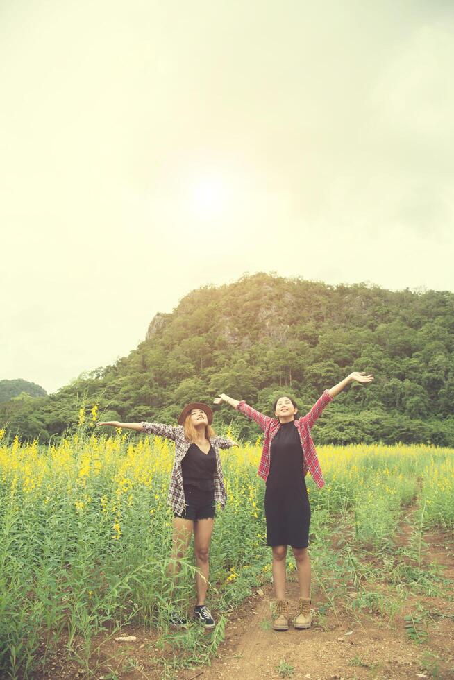 Two hipster woman traveling and raising hands enjoying with flower field together, relaxing good time sunny day. photo