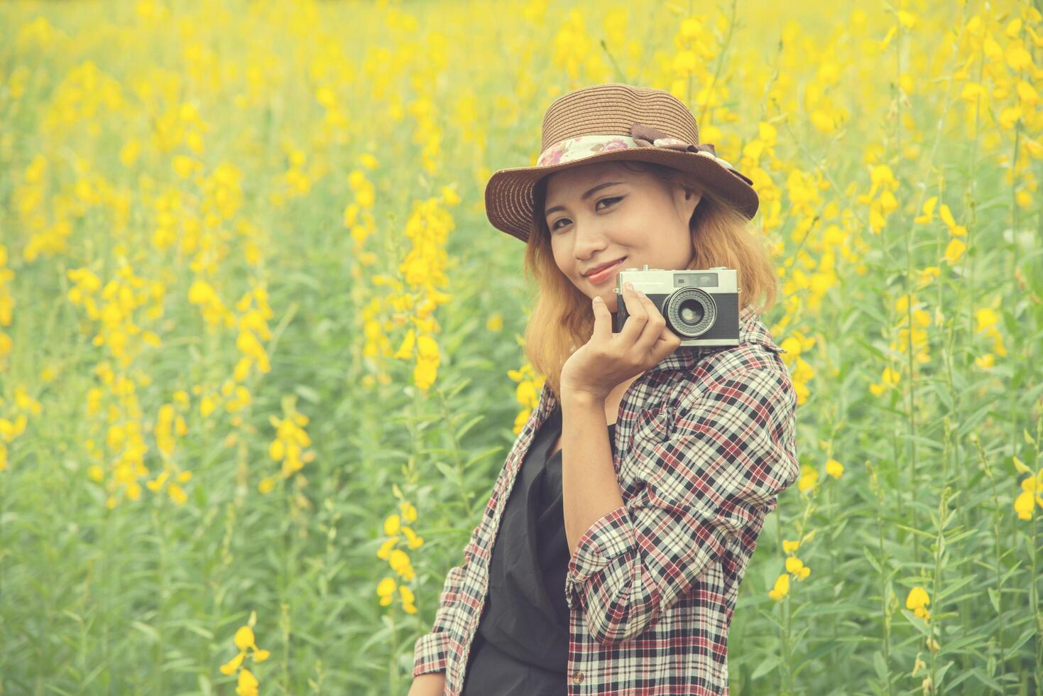 Happy woman in yellow flower field hloding with retro camera outdoors,enjoying nature. photo