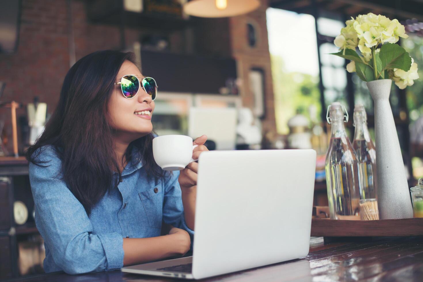 una joven hipster sentada en un café con su laptop, miró hacia otro lado y sonrió feliz, relajándose con las vacaciones, el concepto de estilo de vida de la mujer. foto