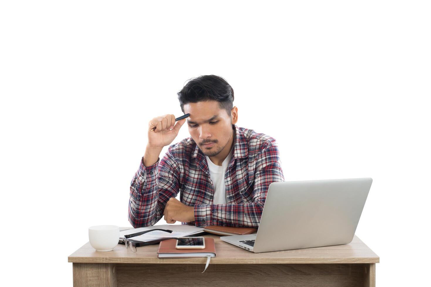 Thoughtful young man holding pen looking at notepad while sitting at his working place. photo