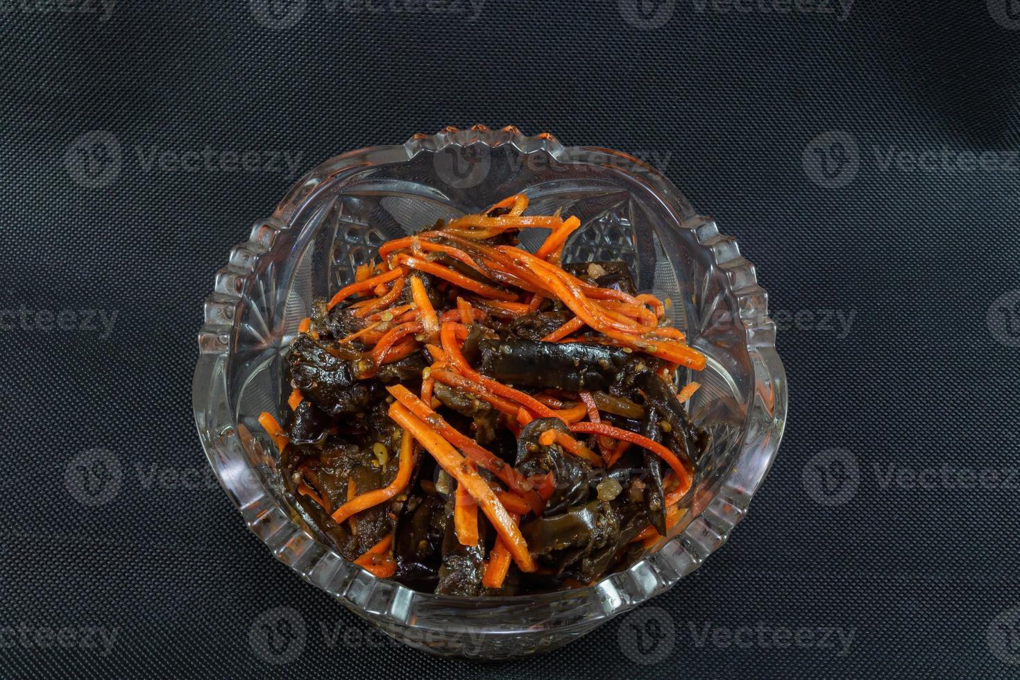 Pickled eggplant with carrots in a plate top view on a black background photo