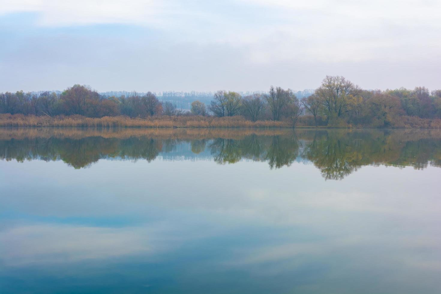 Cold foggy river in the morning with overgrown banks and displaying clouds in the water. photo