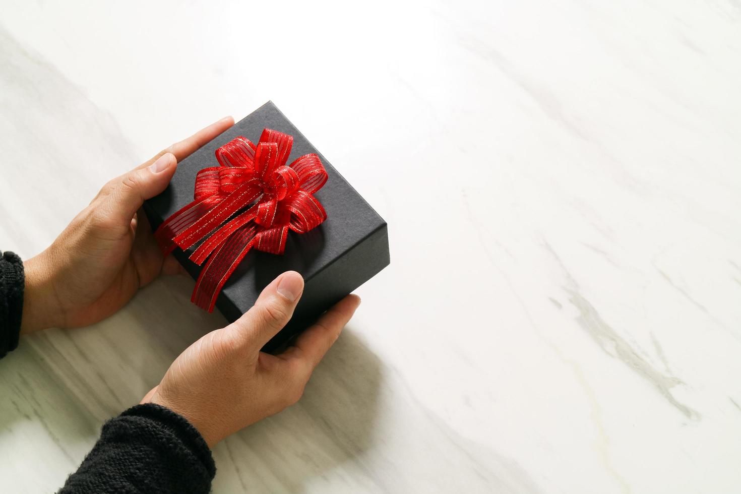 gift giving,man hand holding a gift box in a gesture of giving on white gray marble table background photo