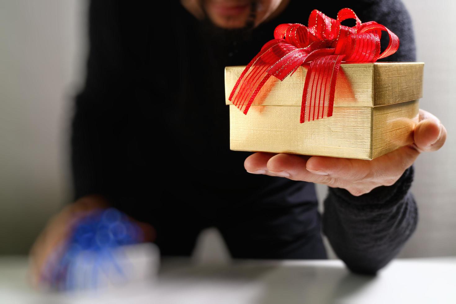 entrega de regalos, mano de hombre sosteniendo una caja de regalo en un gesto de dar. fondo borroso, efecto bokeh foto