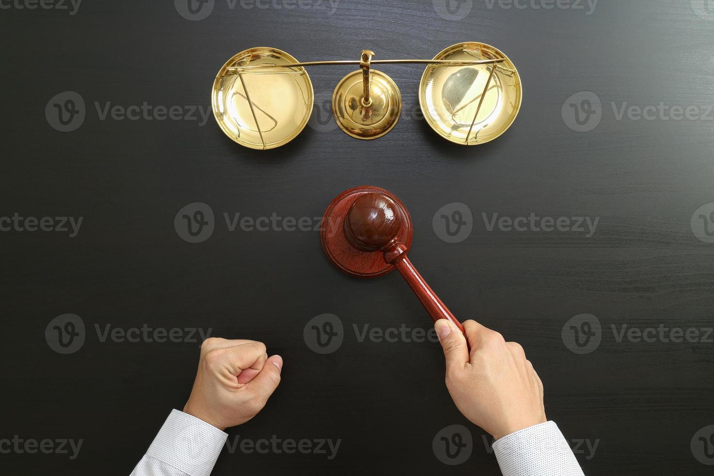 concepto de justicia y derecho. vista superior de la mano del juez masculino en una sala de audiencias con el mazo y la escala de latón en una mesa de madera oscura foto