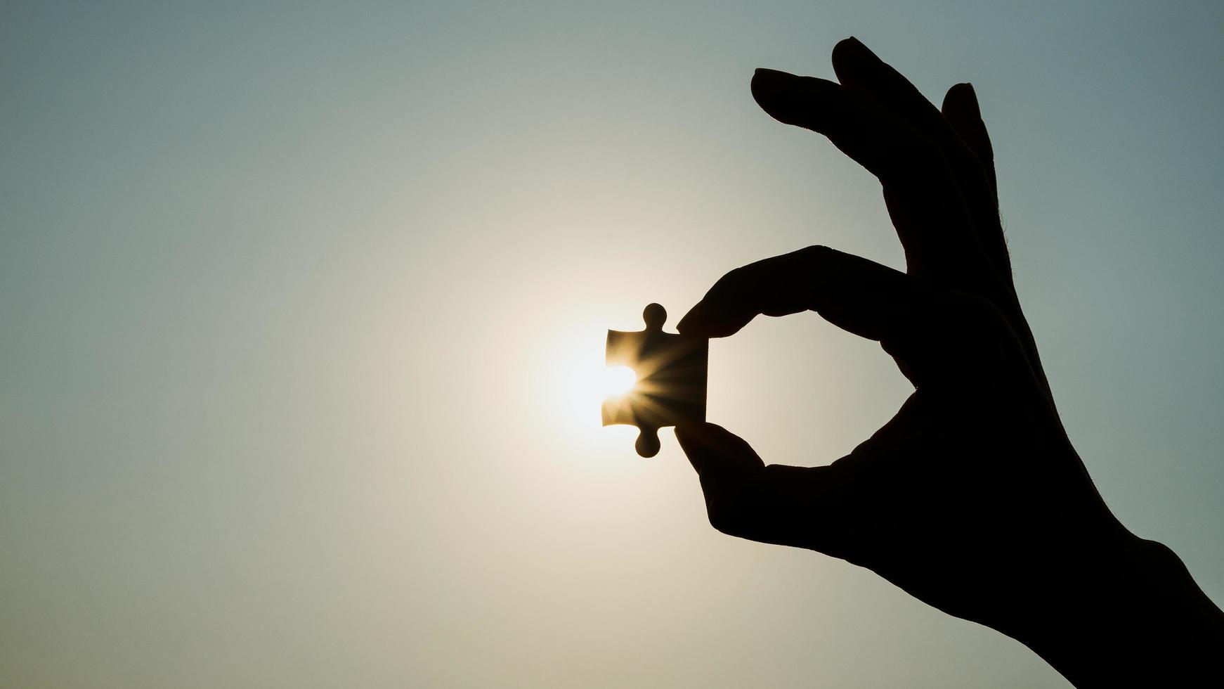 Silhouette closeup of hand holding a piece of jigsaw puzzle over sunlight effect. symbol of association and connection concept. business strategy. photo