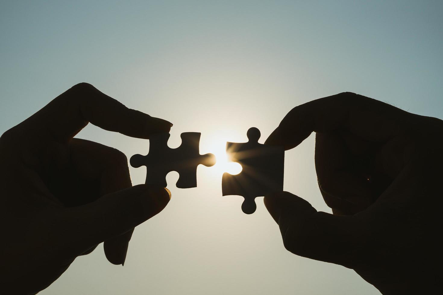 Silhouette of closeup woman and man hand connecting a piece of jigsaw puzzle over sunlight effect. symbol of association and connection concept. business strategy. photo