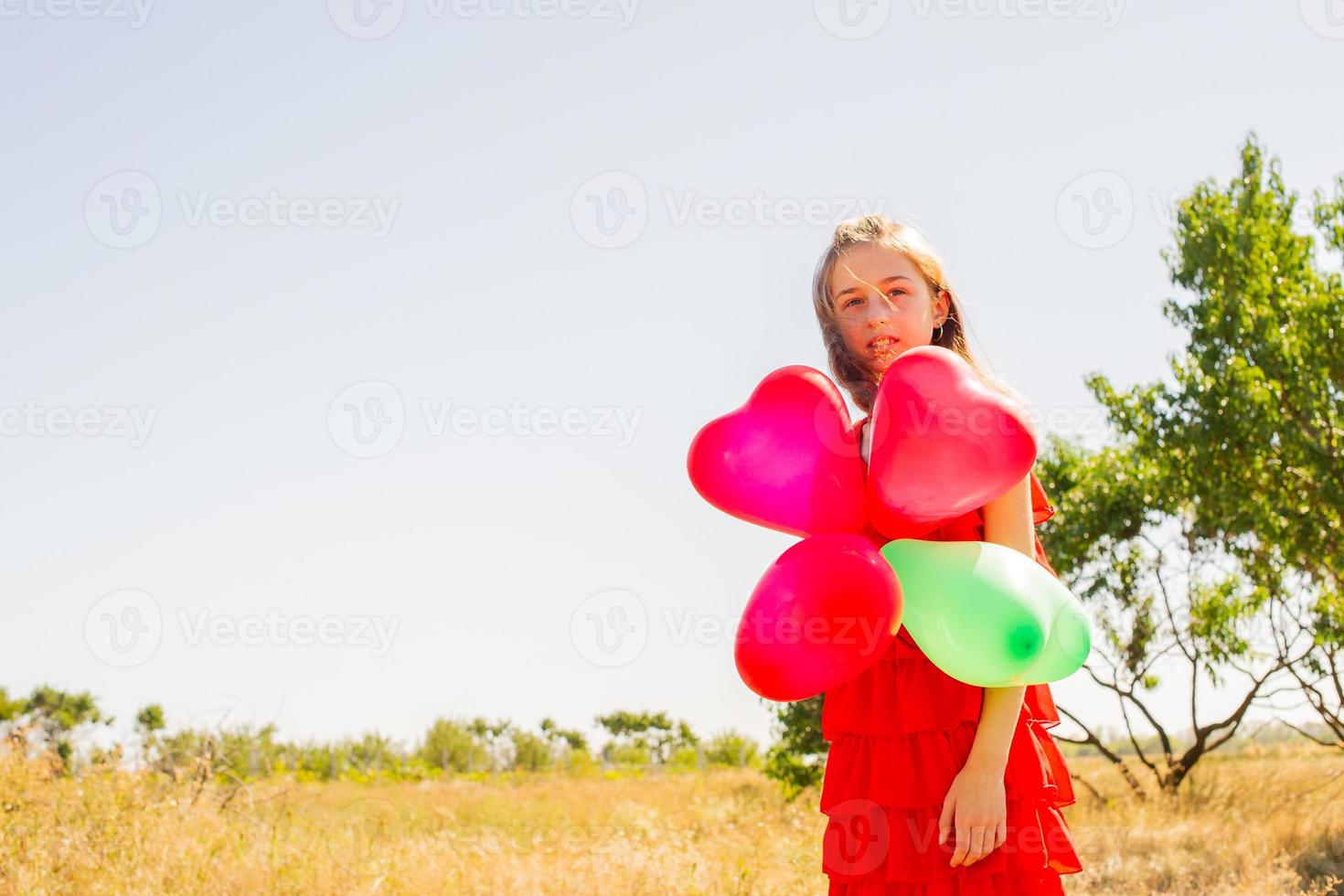 A teenage girl with balloons in a red summer dress against the backdrop of nature on sunny day. photo