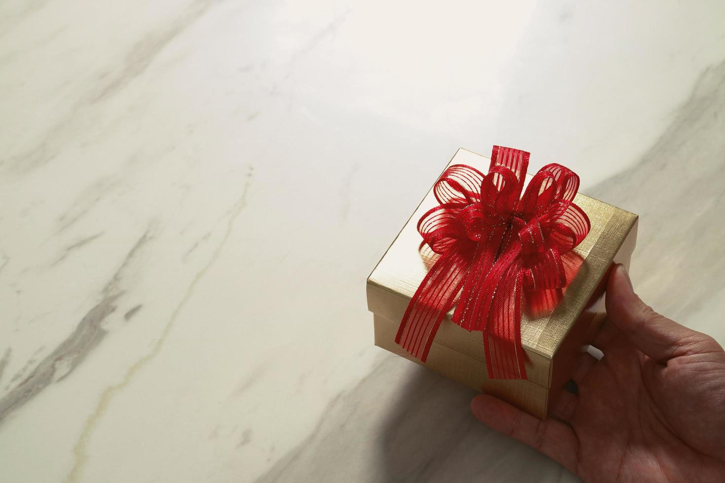 entrega de regalos, mano de hombre sosteniendo una caja de regalo en un gesto de dar en el fondo de la mesa de mármol gris blanco foto