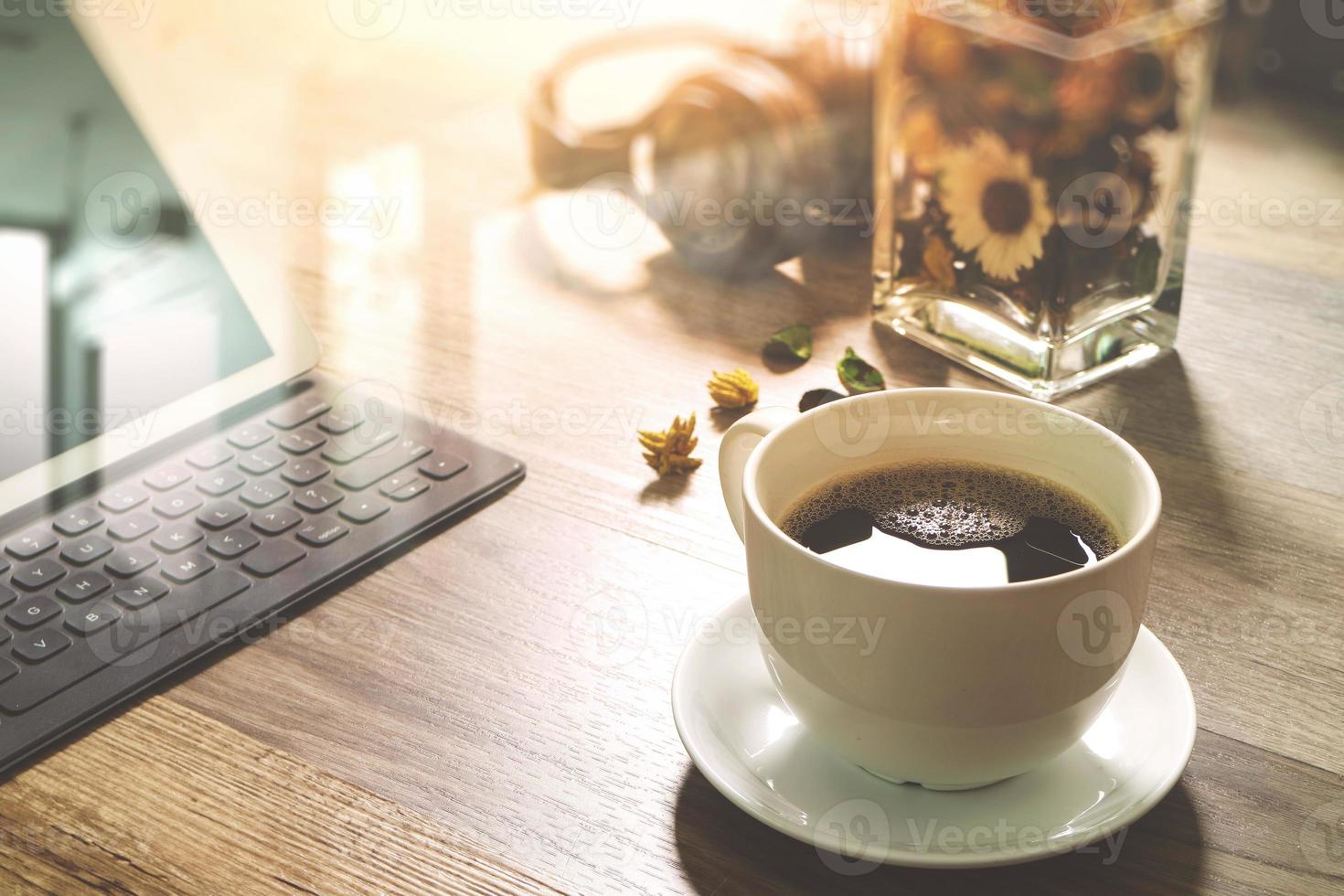Coffee cup and Digital table dock smart keyboard,vase flower herbs,music headphone,eyeglasses on wooden table,filter effect photo