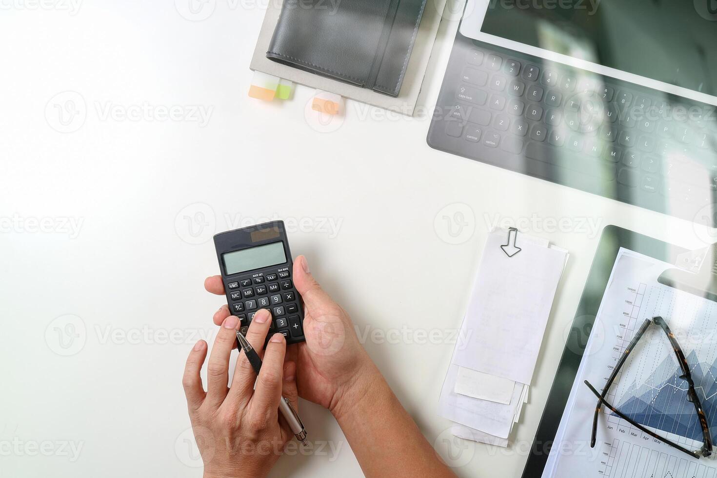 vista superior de la mano de hombre de negocios que trabaja con finanzas sobre costos y calculadora y portátil con teléfono móvil en el escritorio en la oficina moderna foto