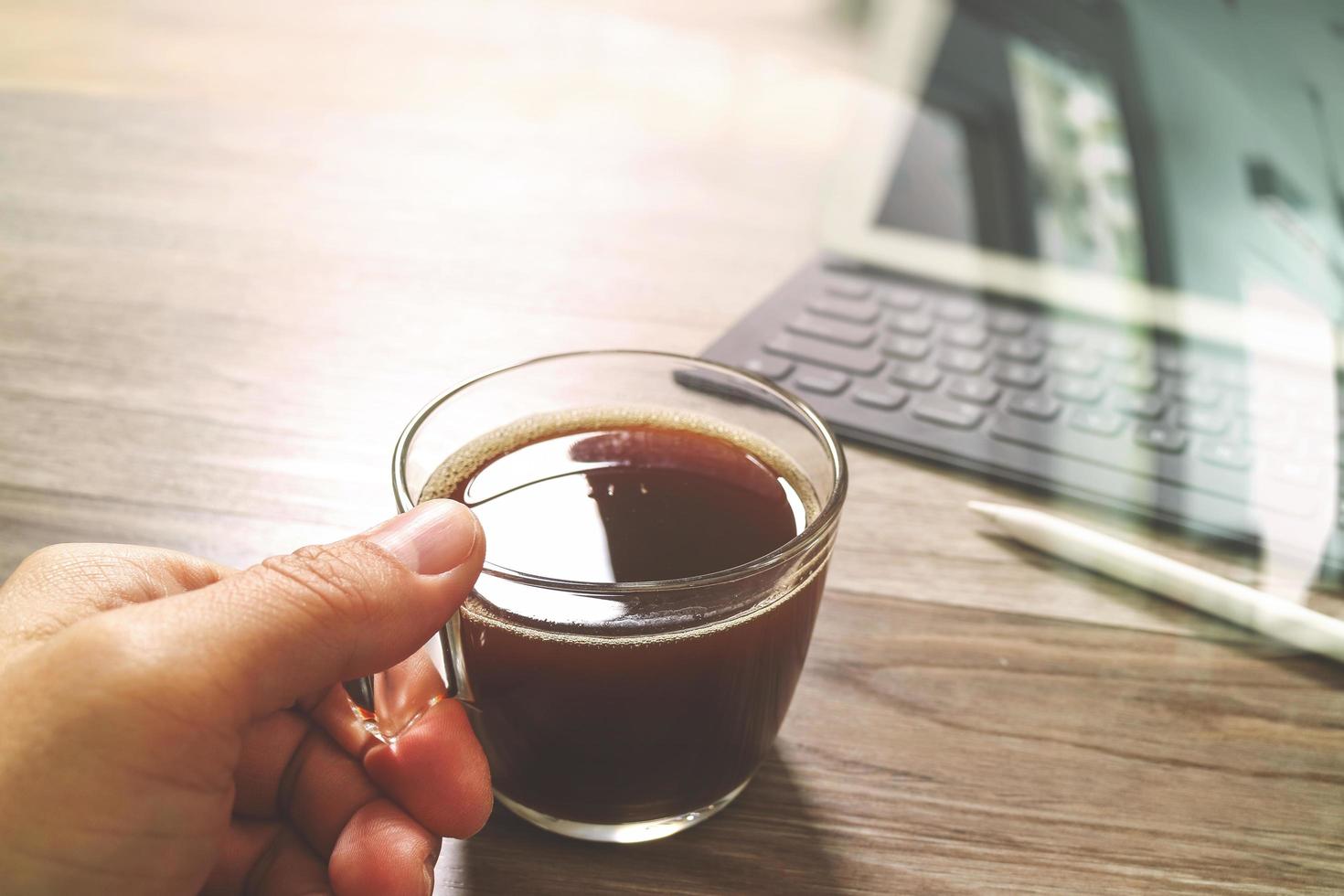 Hand holding Coffee cup or tea and Digital table dock smart keyboard,stylus pen on wooden table,filter effect photo