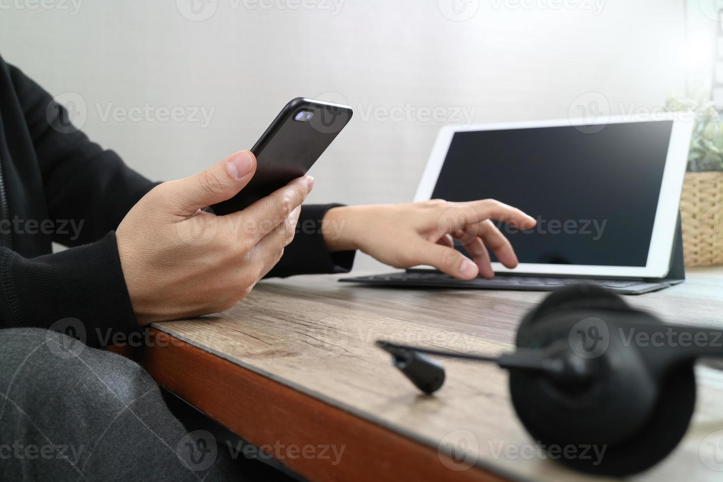 mano de hombre usando auriculares voip con teclado de acoplamiento de tableta digital, teléfono inteligente, comunicación conceptual, soporte de TI, centro de llamadas y servicio de atención al cliente en mesa de madera foto