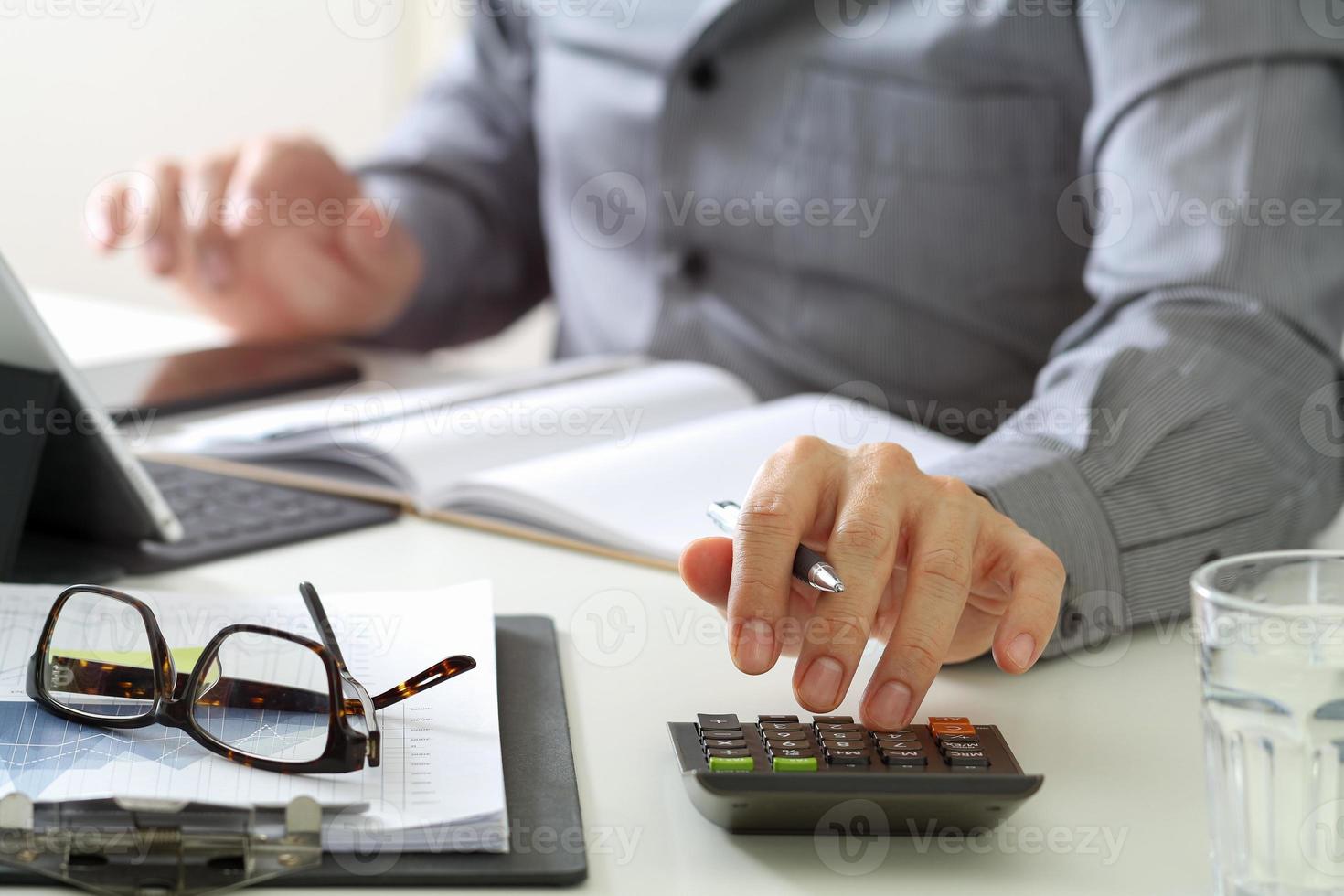 mano de hombre de negocios trabajando con finanzas sobre costos y calculadora y computadora portátil con teléfono móvil en el escritorio en la oficina moderna foto