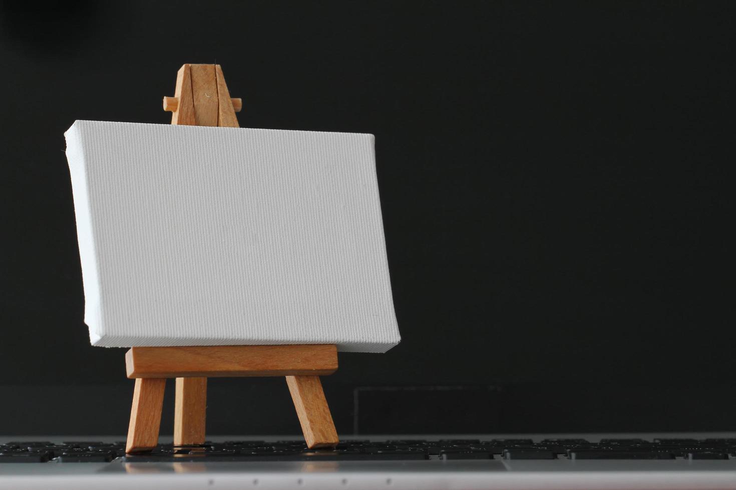 blank canvas and wooden easel on laptop computer as concept photo