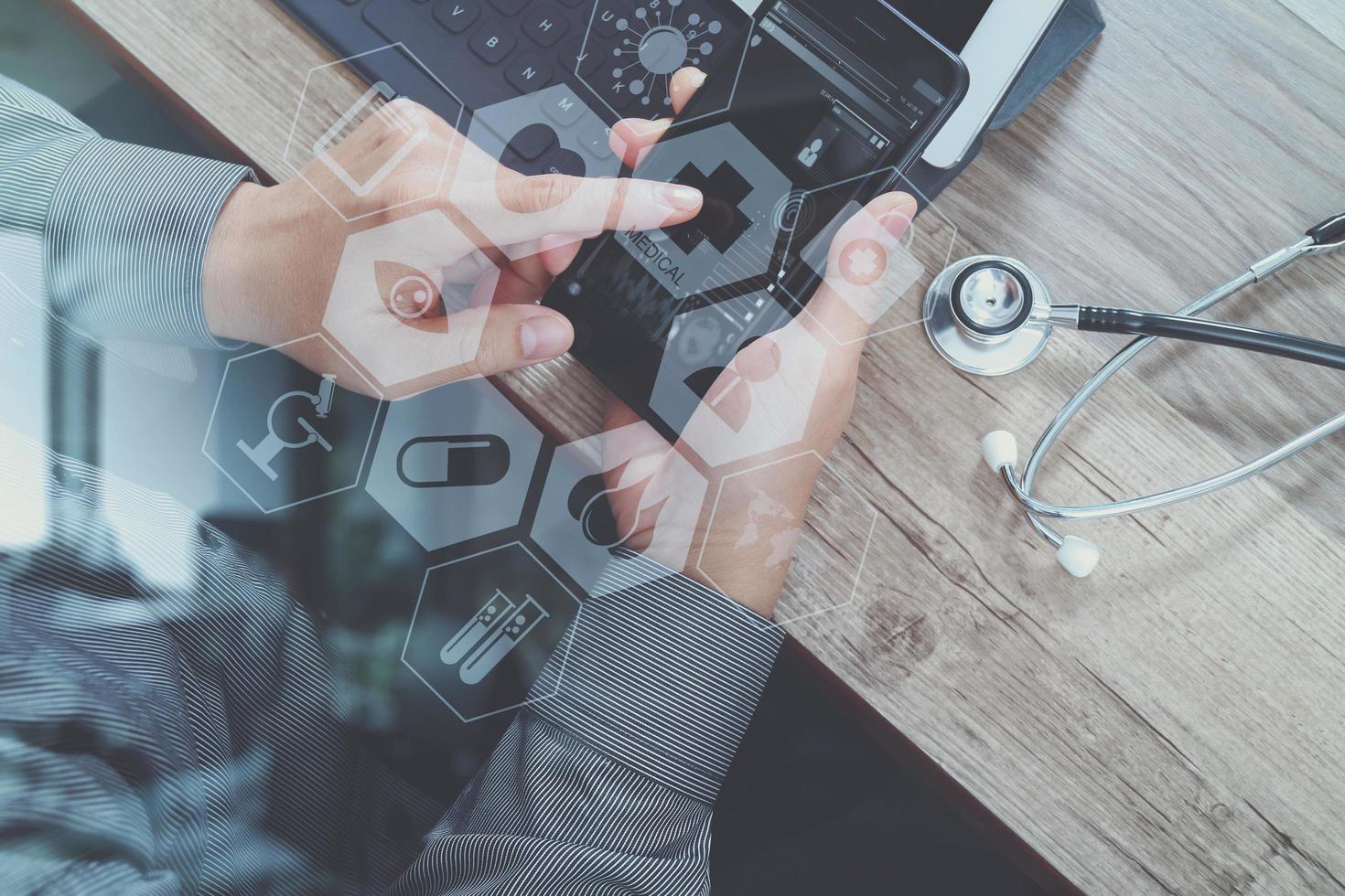 top view of medical doctor hand working with smart phone,digital tablet computer,stethoscope eyeglass,on wooden desk,virtual graphic interface icons screen photo