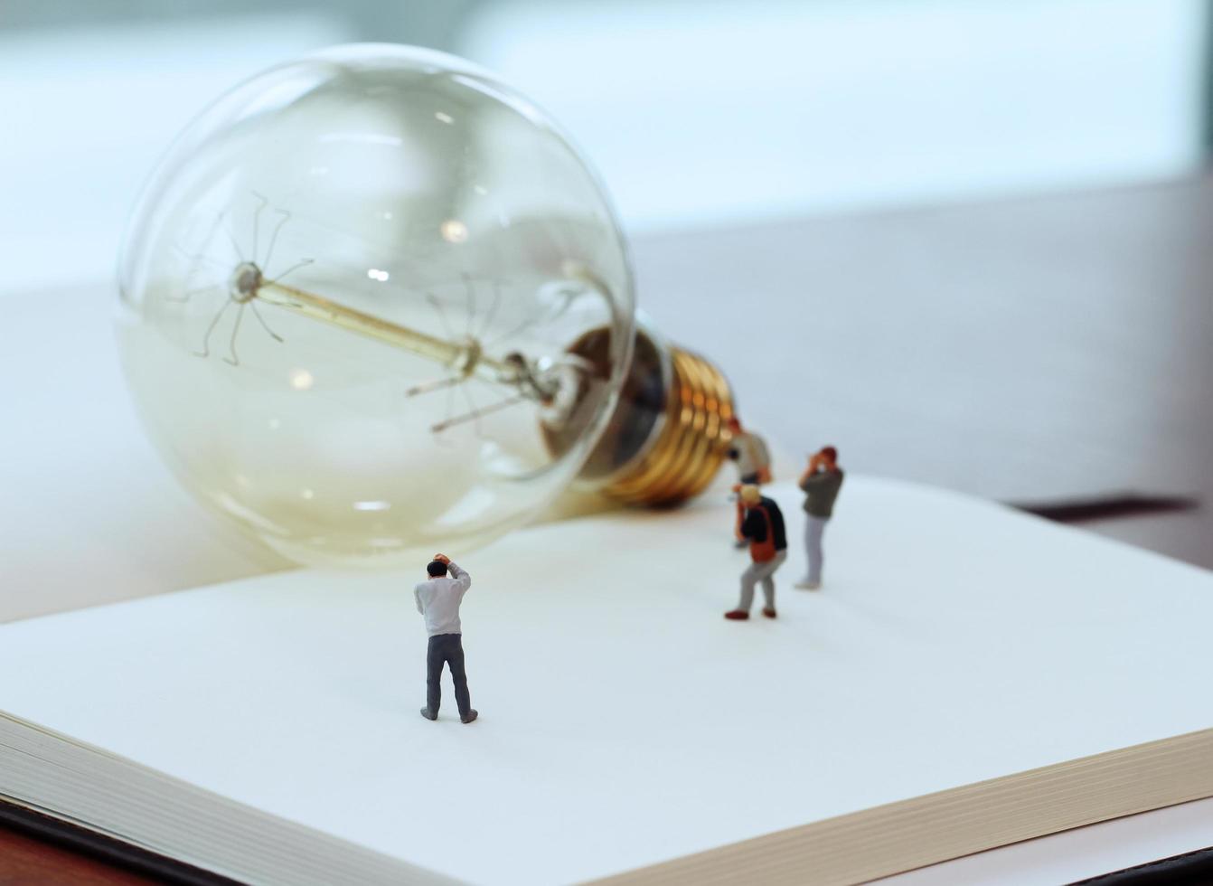 concepto de idea creativa: fotógrafo en miniatura con bombilla vintage en un cuaderno de papel abierto foto