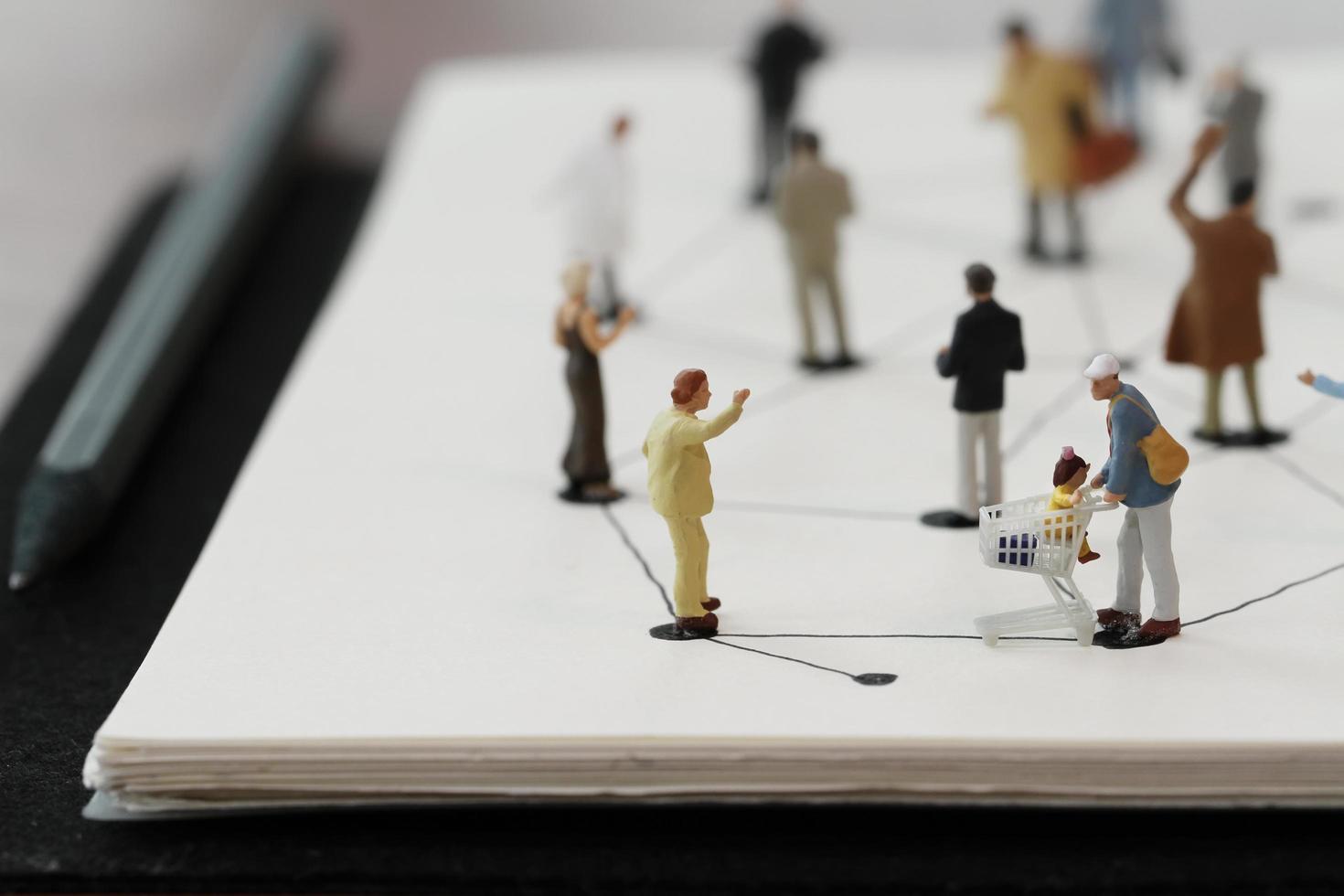 close up of miniature people with social network diagram on open notebook on wooden desk as social media conept photo