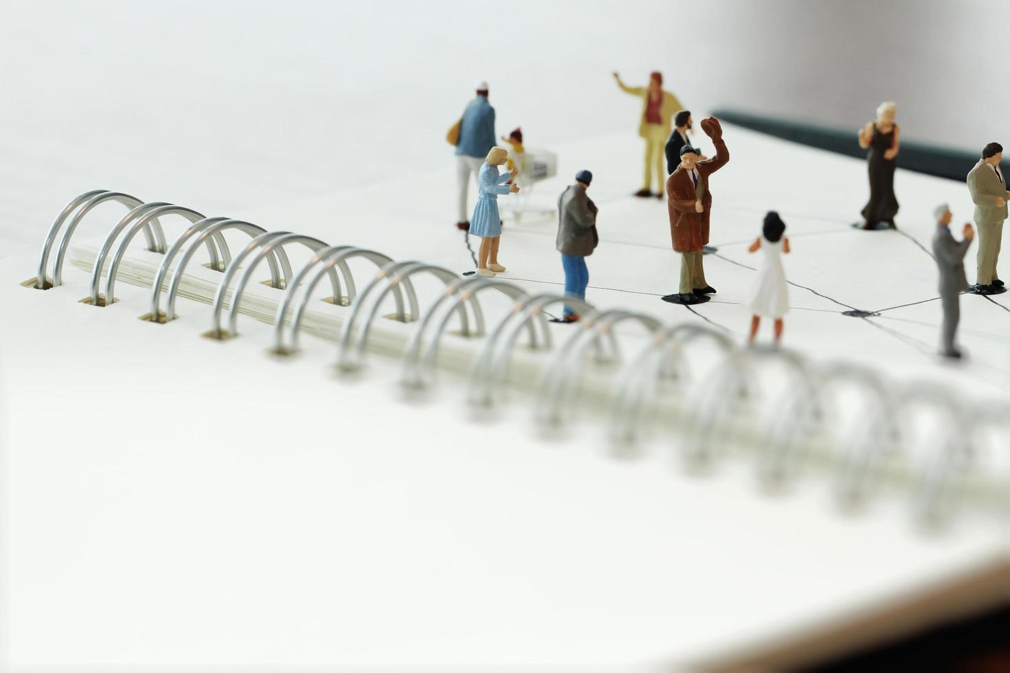 close up of miniature people with social network diagram on open notebook on wooden desk as social media conept photo