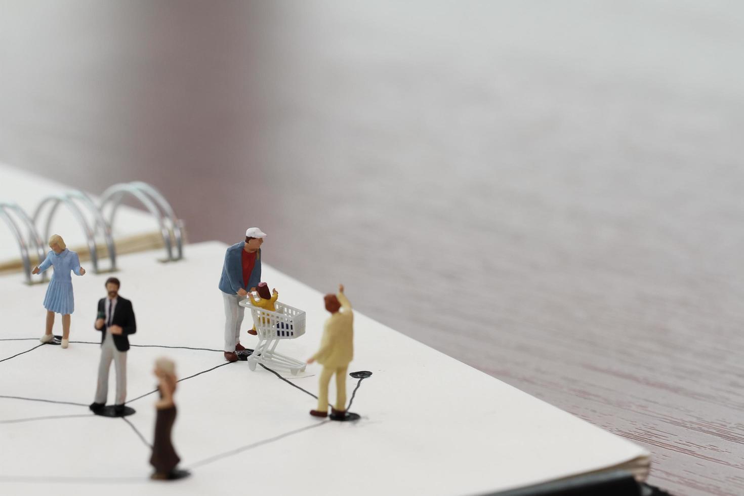 close up of miniature people with social network diagram on open notebook on wooden desk as social media conept photo