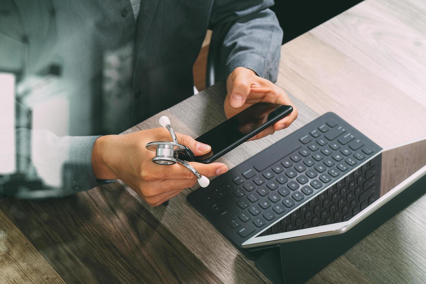 top view of medical doctor hand working with smart phone,digital tablet computer,stethoscope eyeglass,on wooden desk,filter photo