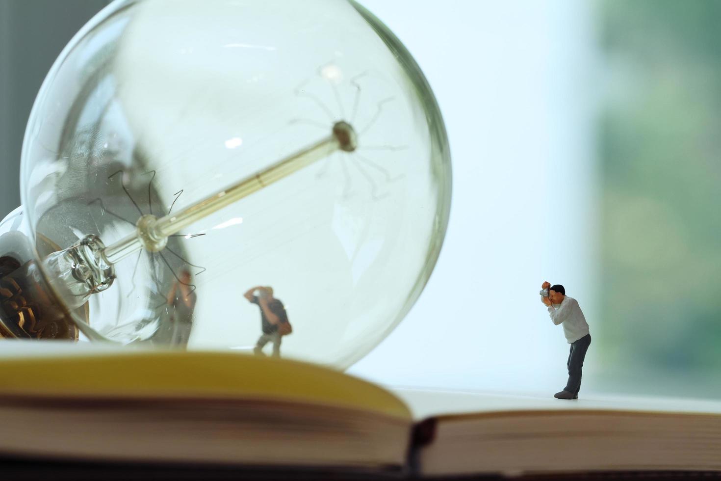 Creative idea concept - miniature photographer with vintage light bulb on open paper notebook photo