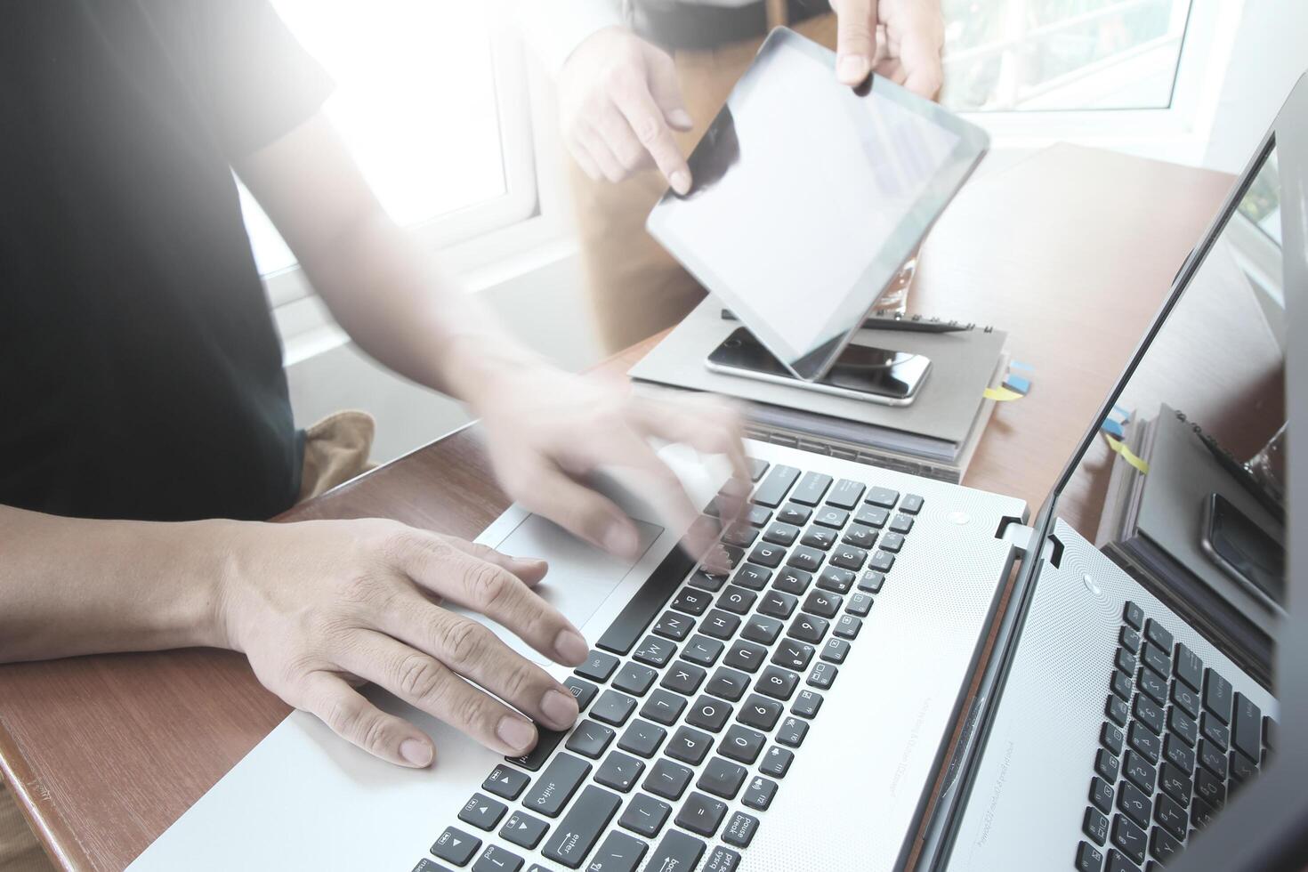 business documents on office table with smart phone and laptop computer and two colleagues discussing data in the background photo