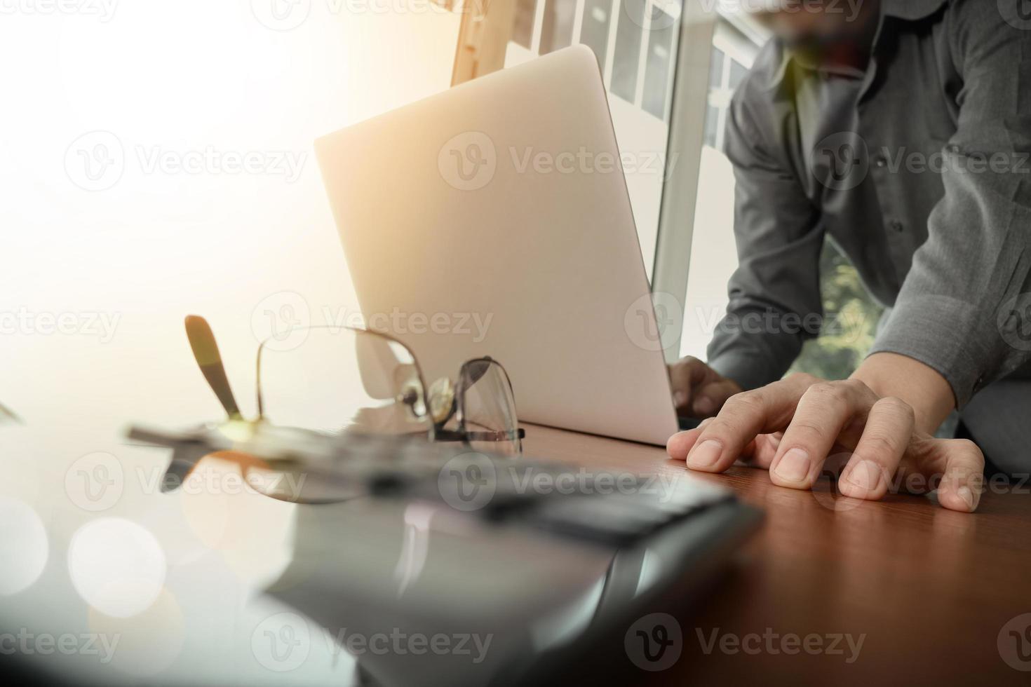 businessman hand working with new modern computer and smart phone and business strategy on wooden desk with calculator and eye glasses foreground as concept photo