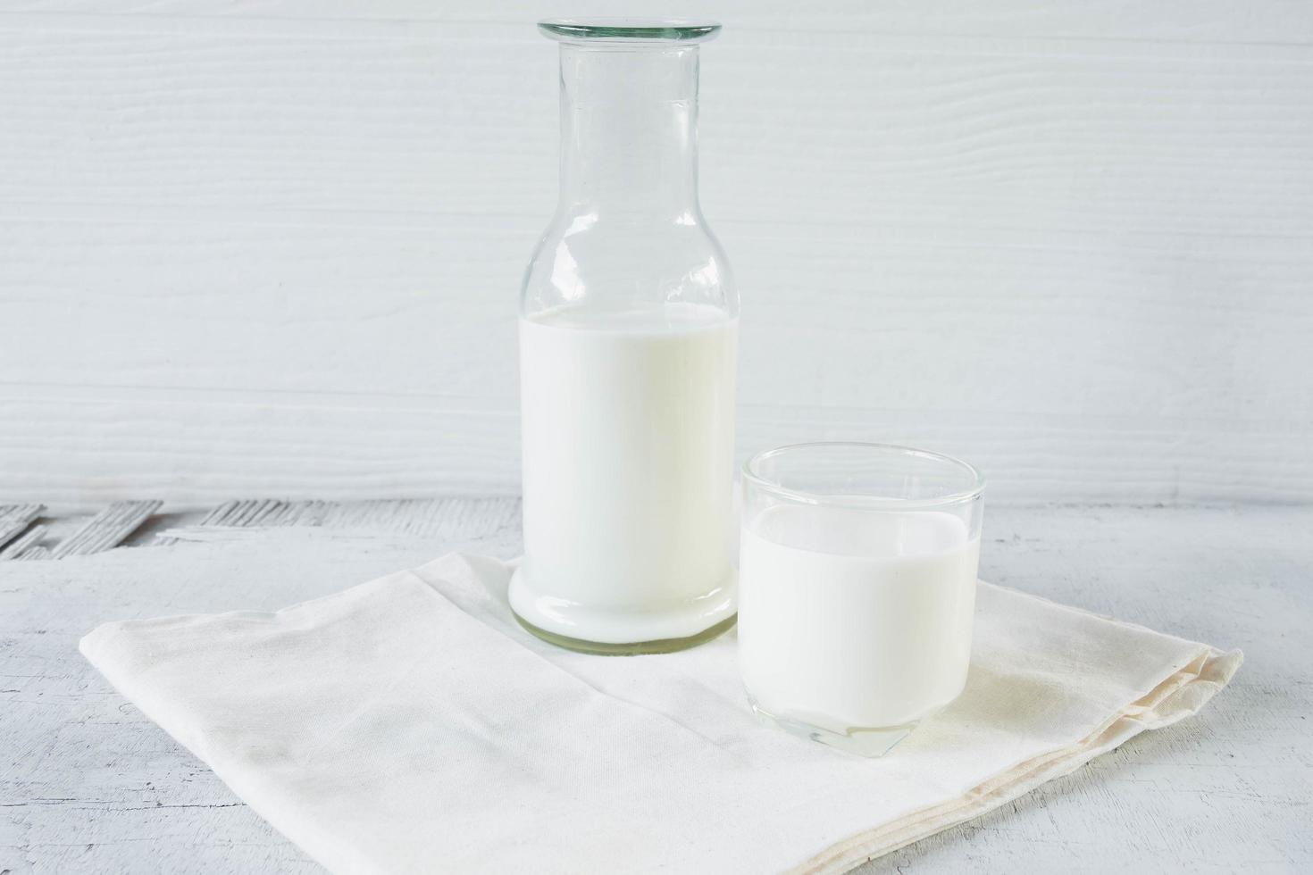 leche en vaso y botella de leche sobre fondo blanco de madera foto