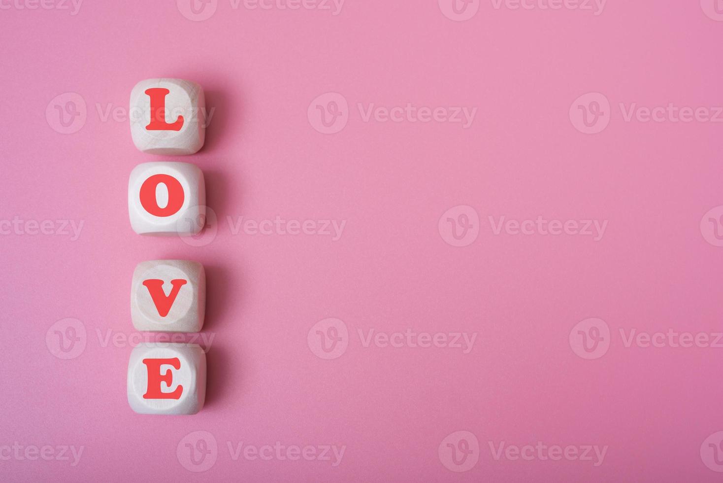 The word love is in the shape of a heart on wooden cubes on a pink background. photo