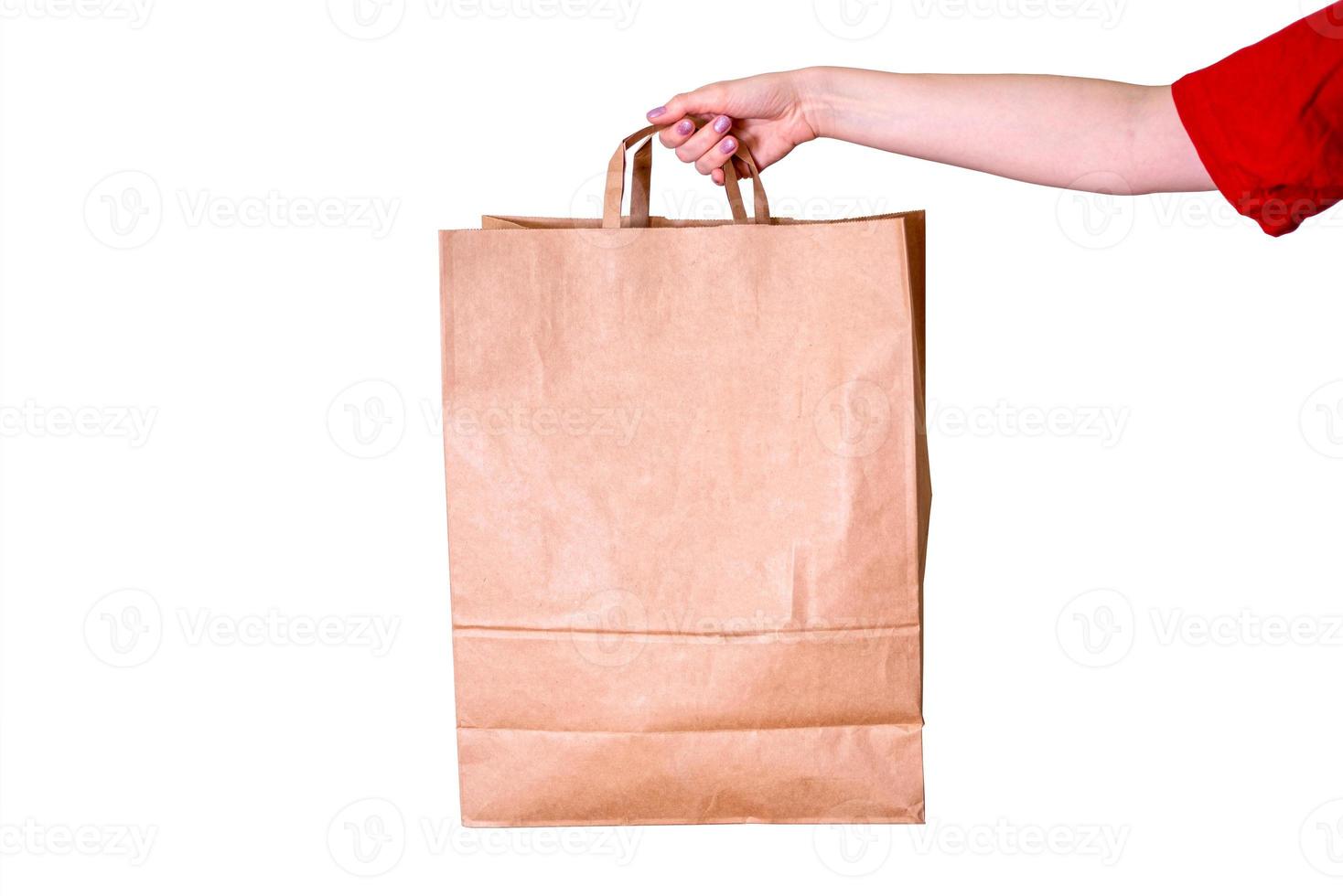 A woman's hand holds an empty kraft paper bag isolated on a white background. photo
