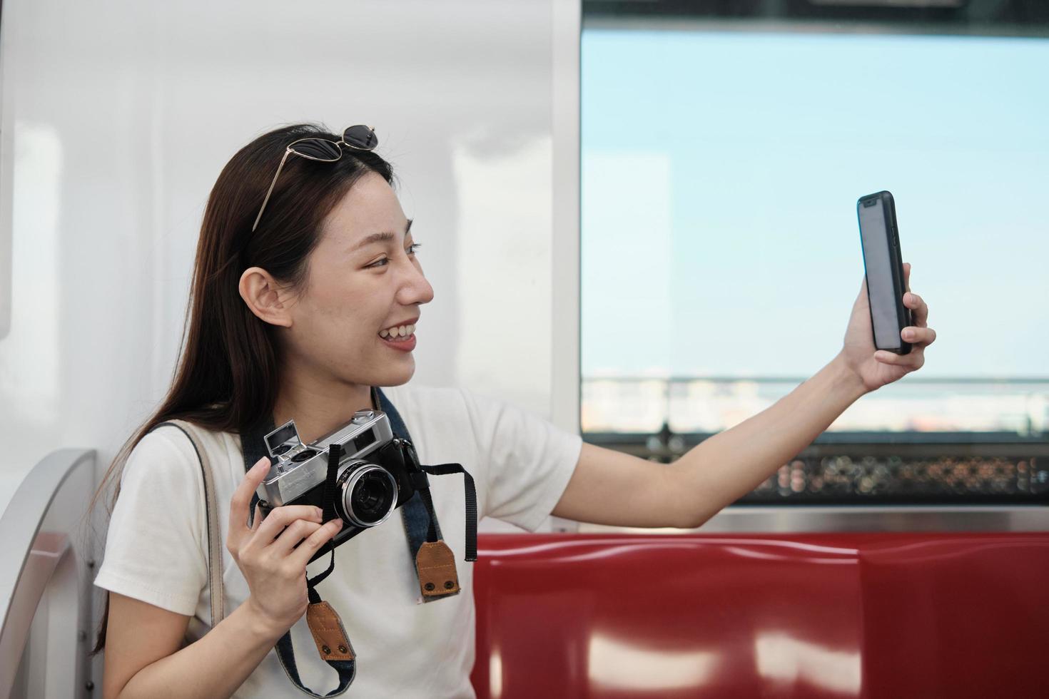 Young beautiful Asian female tourist online chatting, mobile phone video call, check-in, and social media posting, travel urban train transport, city passenger lifestyle, happy journey vacation trip. photo