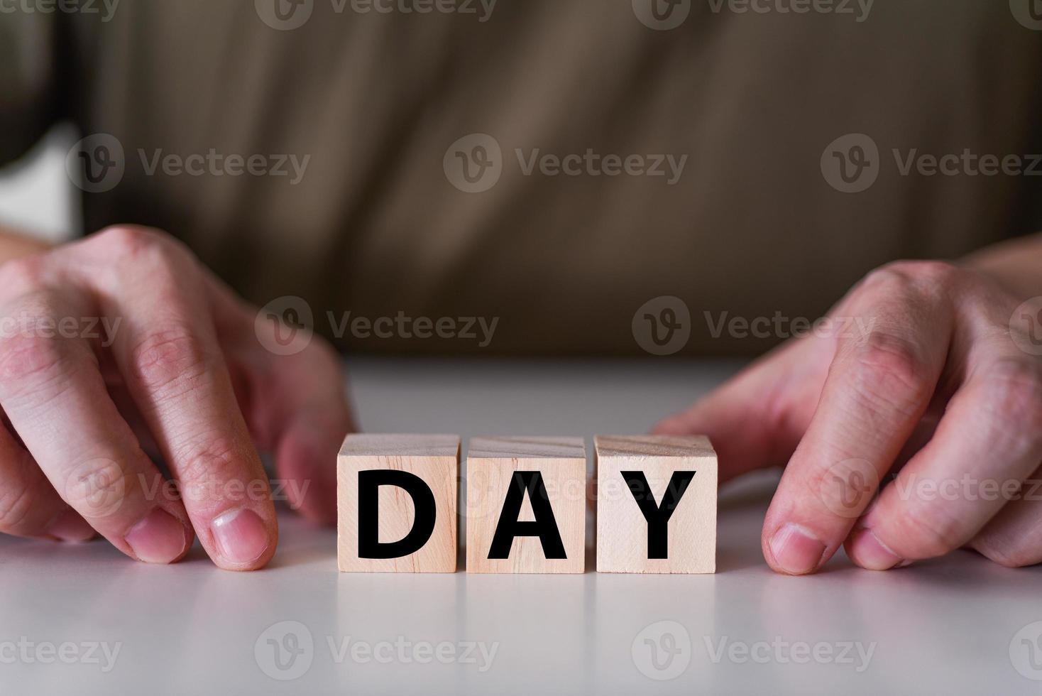 A businessman holds wooden cubes with the word day. photo