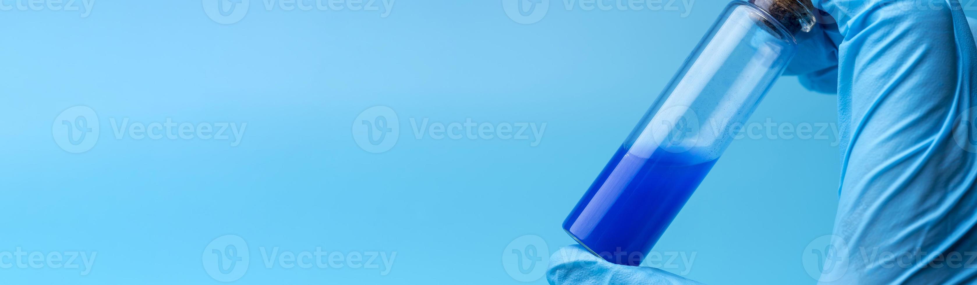 Close-up of glass tube with blue fluid in scientist hand during medical test photo