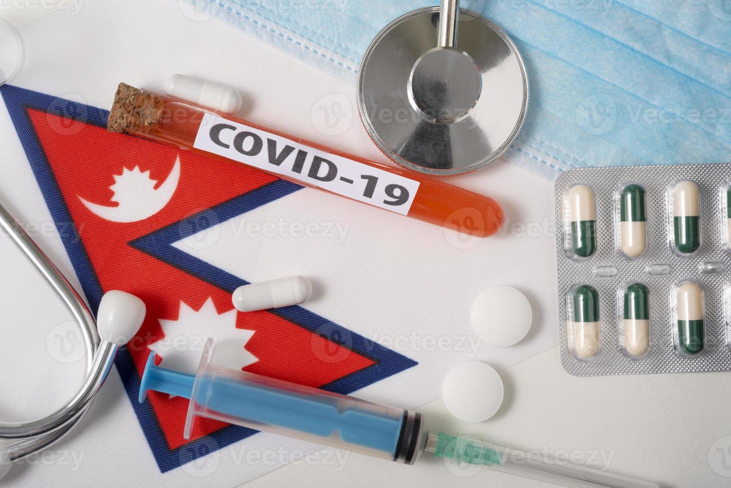 Coronavirus, the concept COVid-19. Top view protective breathing mask, stethoscope, syringe, tablets on the flag of Nepal. photo