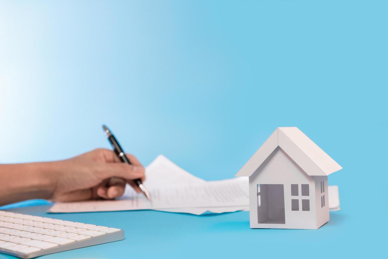 White house model and man hand signing contract for buy and sale house in blue background for refinance plan and real estate concept. photo