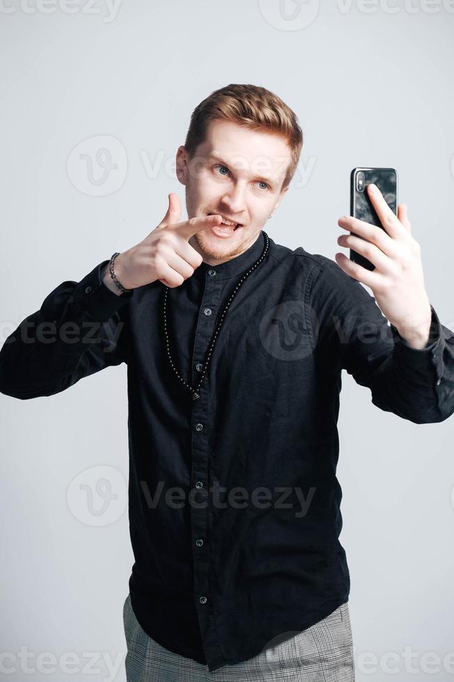 Young man in a black shirt with a smartphone in his hands on a white background. Copy, empty space for text photo