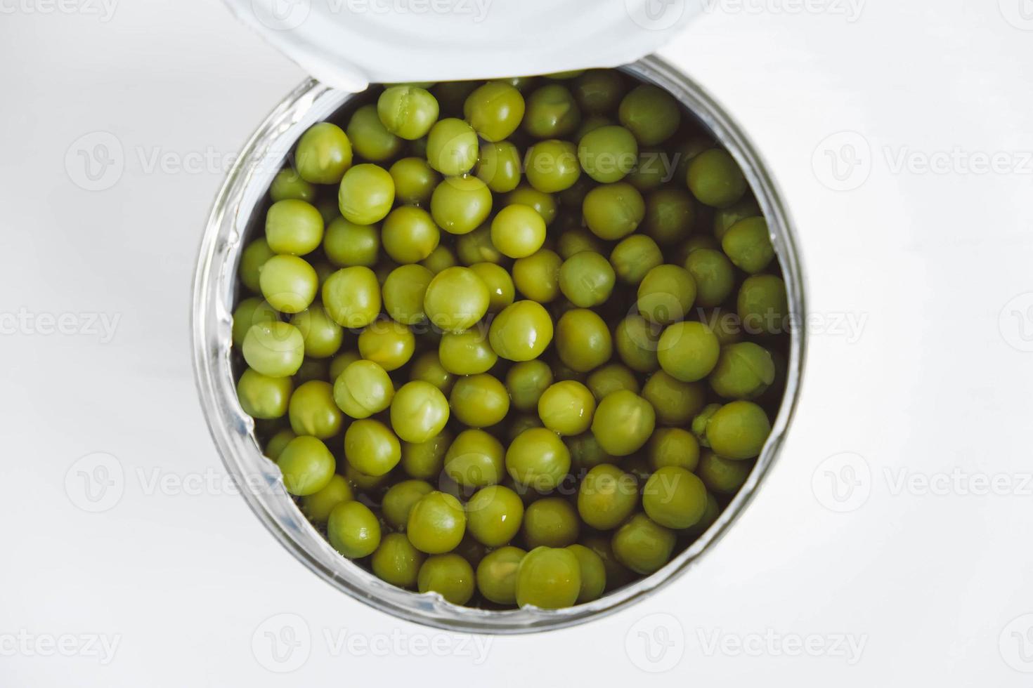 guisantes dulces verdes enlatados en una lata de metal de aluminio abierta sobre una mesa blanca. vista superior. copiar, espacio vacío para texto foto