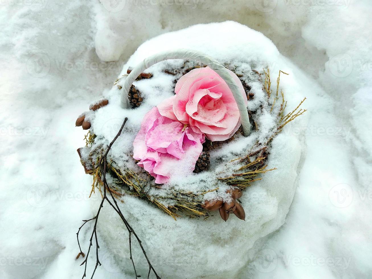 Paper pink roses in a wicker basket from a tree vine, covered with snow. photo